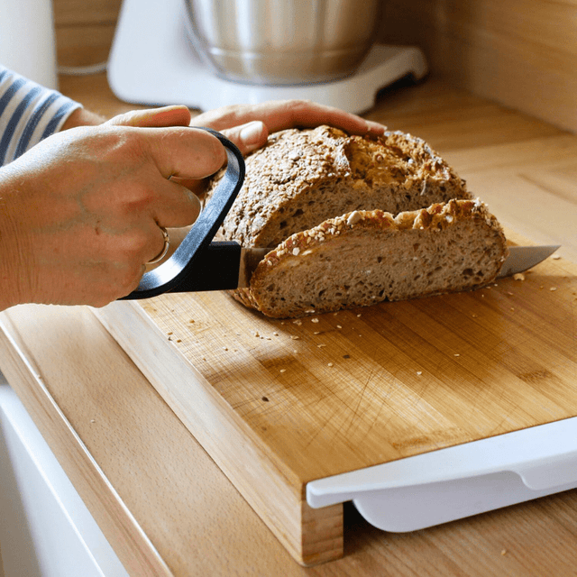 Person skär en skiva fullkornsbröd med den ergonomiska brödkniven på en träskärbräda