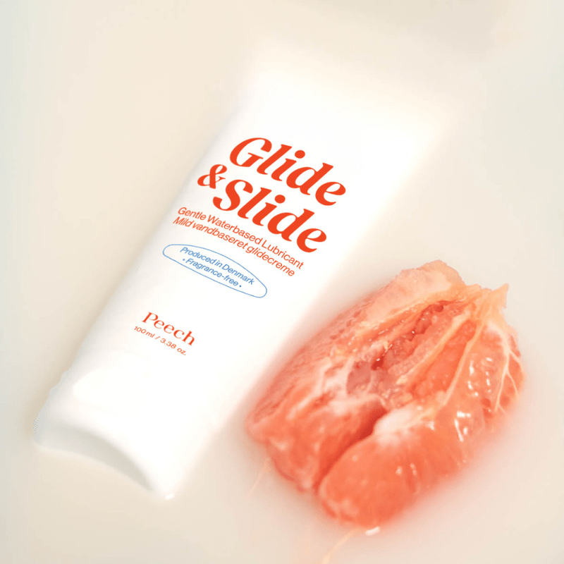 Vit tub med Peech Glide & Slide glidmedel ligger bredvid en halverad grapefrukt