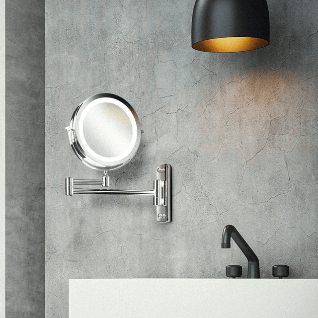 Væghængt makeup-spejl i krom med LED-lys på en grå betonvæg over en hvid vask i et badeværelse