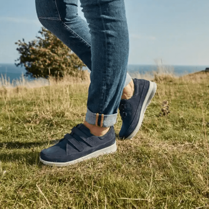 Ett par mörkblå New Feet damskor med kardborreband på en person som går i gräset utomhus