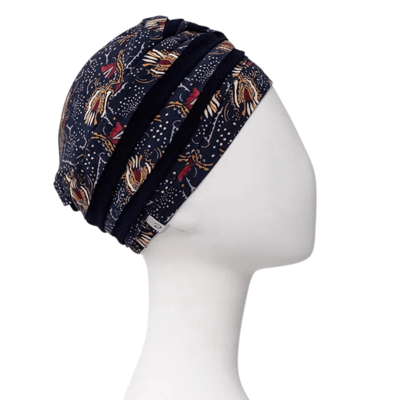 Shanti turban i Amber Garden-design med mörkblå botten och varma mönster, sedd från höger sida med etikett