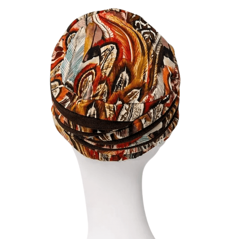 Shanti turban med detaljerat Tribal Feathers mönster i varma färger, sedd bakifrån på en vit skyltdocka