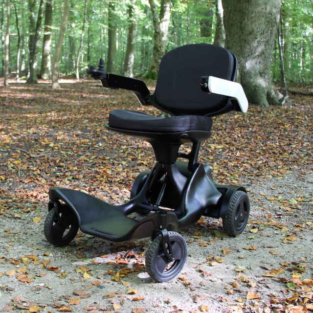 Zeno2 hopfällbar elrullstol i svart placerad på en stig i en skog med löv på marken