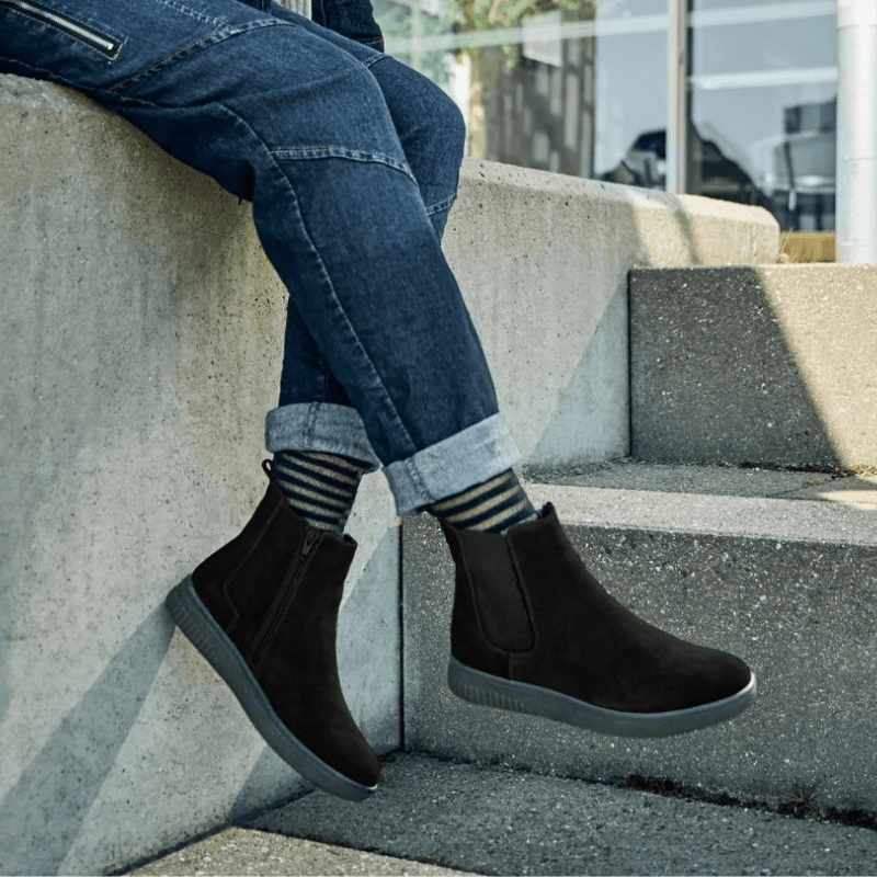 Person med Green Comfort damkängor i svart mocka, jeans och randiga strumpor på betongtrappa