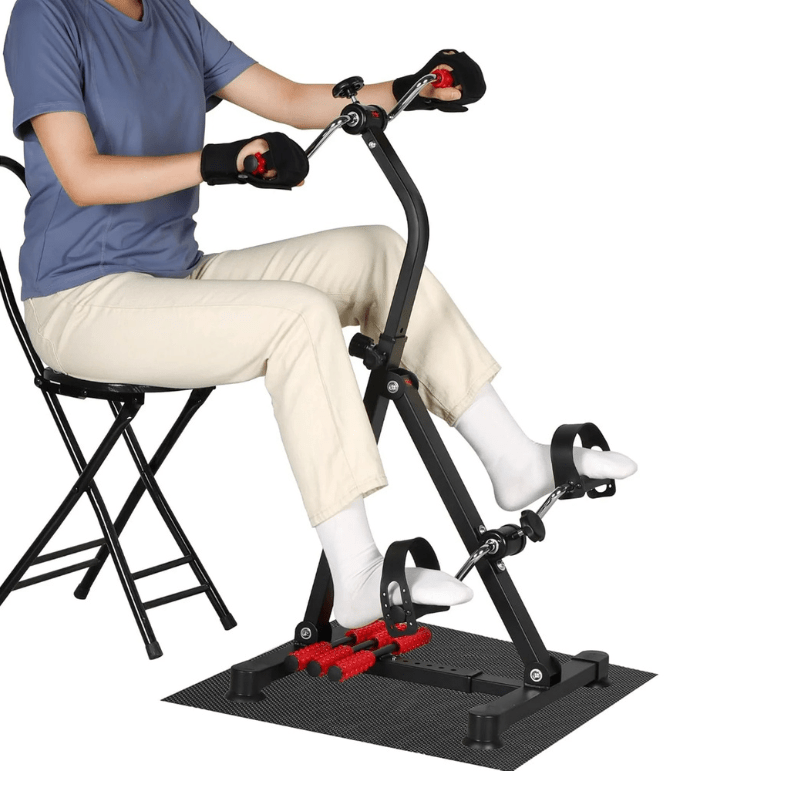 En person använder pedaltränaren för armar och ben sittande på en stol, med fötterna på massagerullarna