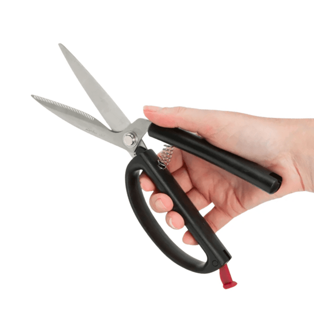 En hand håller en självöppnande kökssax med svarta handtag och öppna blad