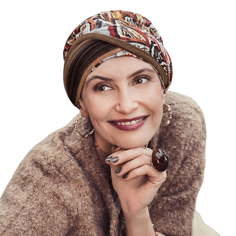 Kvinna bär en Shakti turban i mönstret Tribal Feather med varma höstfärger och fjädrar, leende och tittar åt sidan