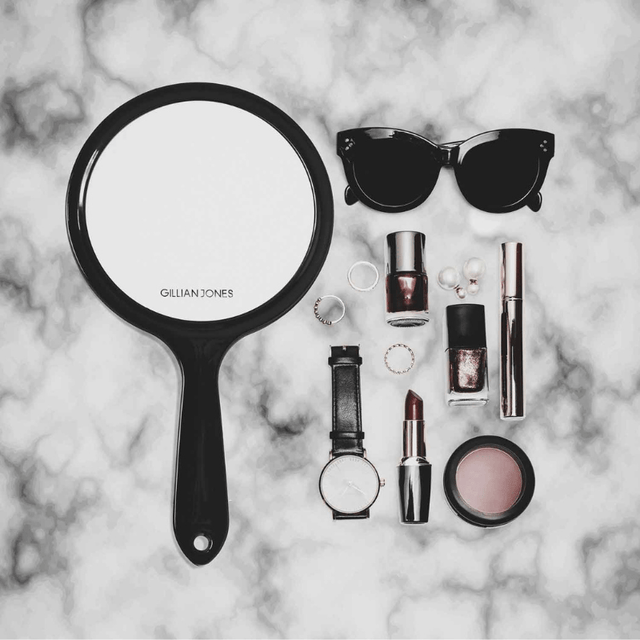 Gillian Jones håndspejl omgivet af makeup og accessories på en hvid marmoroverflade