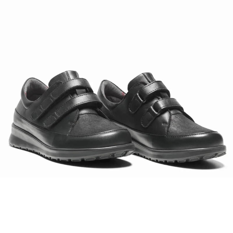 Ett par svarta New Feet damskor med kardborreband, sedda snett framifrån
