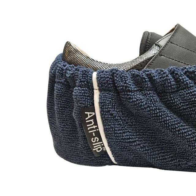 Närbild på ett mörkblått halkskydd till skor med "Anti-slip"-etikett, fäst på en mörk sko med metallisk detalj