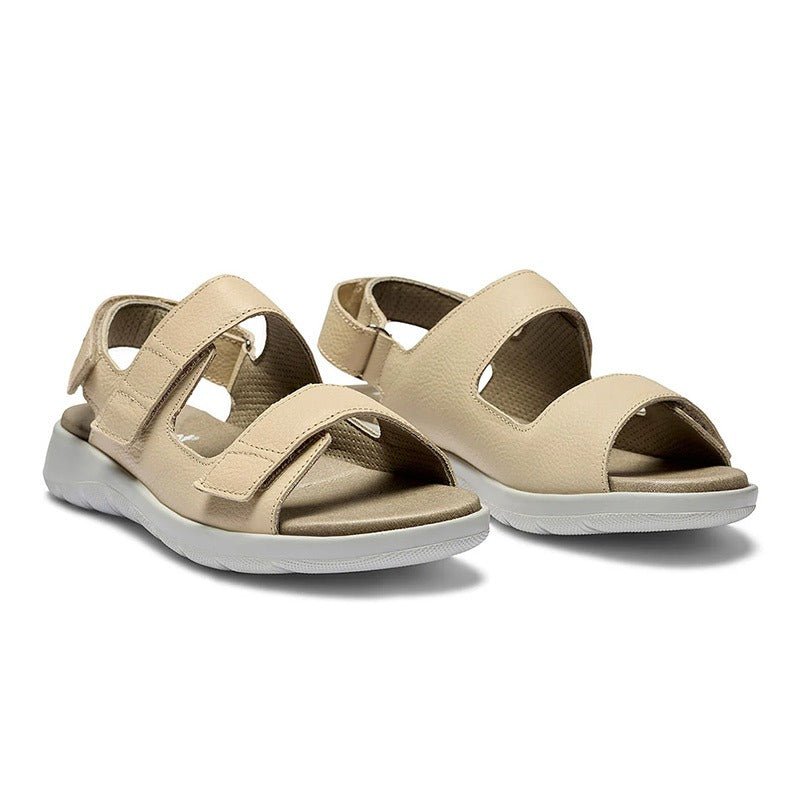 Ett par sandfärgade New Feet damsandaler i kalvskinn med kardborreband, sedda snett framifrån