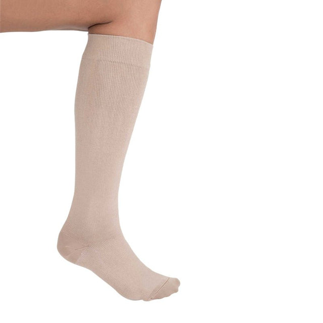 En beige knähög stödstrumpa med ribbad yta, sedd från sidan på ett böjt ben
