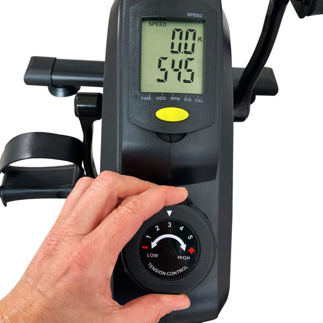 Närbild på en hand som justerar motståndet på pedaltränaren, med digital display som visar träningsdata
