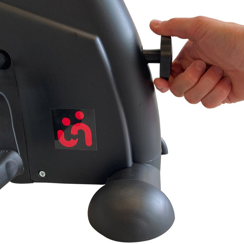 En hand som justerar motståndet på den svarta digitala pedaltränaren med ett skruvhandtag