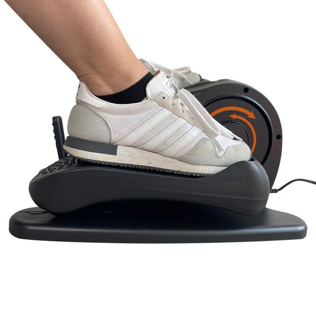 En fot i vit sneaker på pedalen av en svart elektrisk elliptisk tränare, sedd från sidan