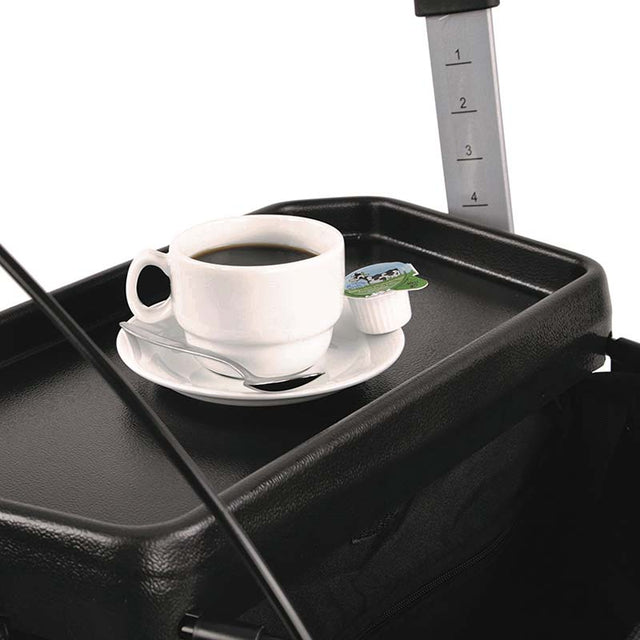 Närbild på rullatorns bricka med en vit kaffekopp, fat och sked, samt en mjölkförpackning