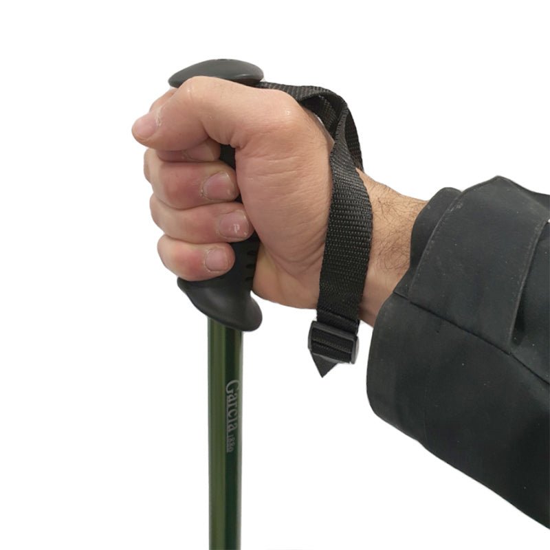 En hand som håller den gröna vandringsstavens svarta handtag med handledsrem, i användning