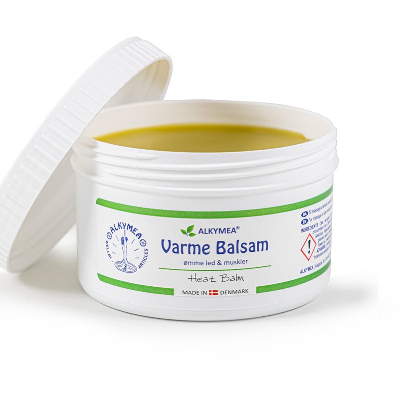Närbild av Alkymea Värmebalsam i öppen vit burk, locket ligger bakom och den gula salvan syns tydligt