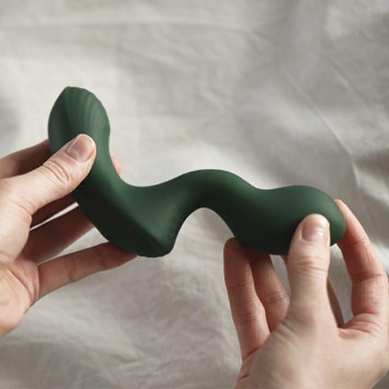 Två händer håller och böjer den mörkgröna Birch prostatavibratorn för att visa dess flexibilitet