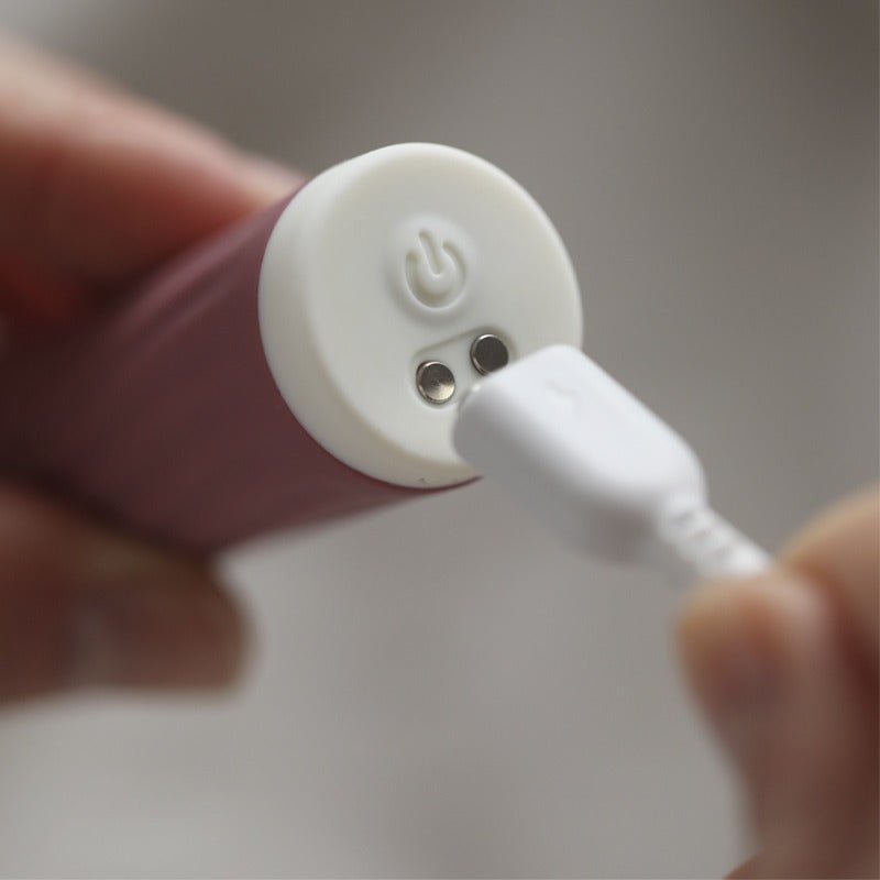 Närbild på Bullie vibratorns vita bas med laddningskontakter och strömknapp, en laddare ansluts