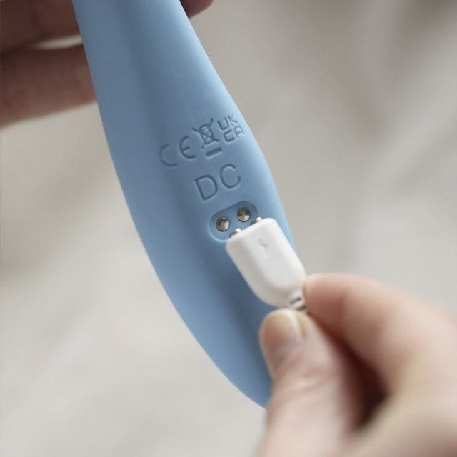 Närbild på den blå Penny vibratorns laddport där en vit USB-laddare ansluts
