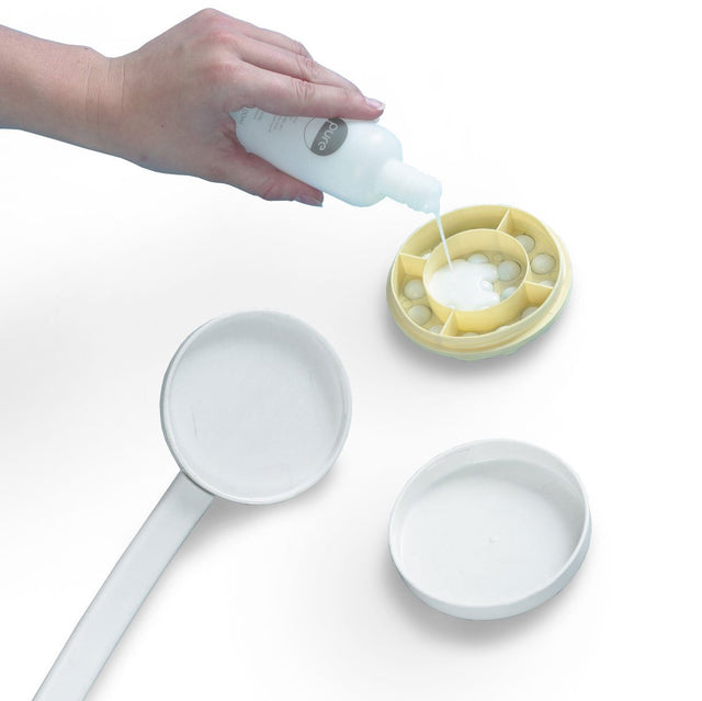 Närbild på en hand som fyller lotionapplikatorns gula fack med vit lotion