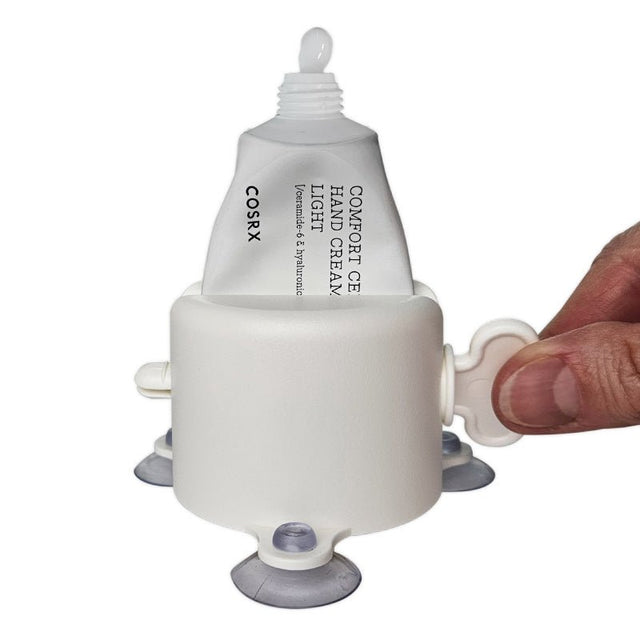 Vit tubklämma med sugproppar i användning, en hand pressar ut kräm ur tuben