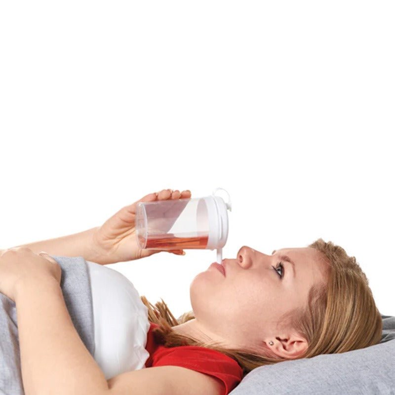 En kvinna ligger ner och dricker ur en transparent pipmugg med röd dryck