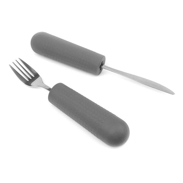 Två grå halksäkra grepp för bestick, ett på en gaffel och ett på en kniv, liggandes på vit bakgrund
