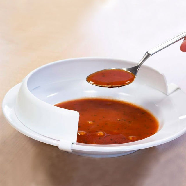 Pet-emot-kant i vit plast fäst på en tallrik med röd soppa, en sked skopar upp mat