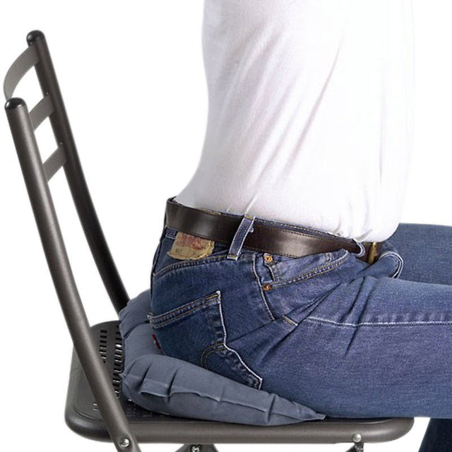 En person sitter på en mörkgrå uppblåsbar sittkudde som avlastar trycket på en stol