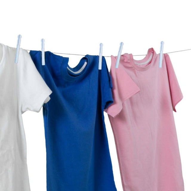 Vita klädnypor som håller upp en vit, blå och rosa t-shirt på ett klädstreck
