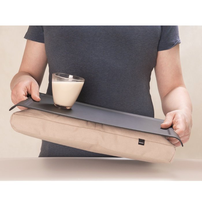 Person bär bricka med kudde och ett glas mjölk, visar de ergonomiska handtagen