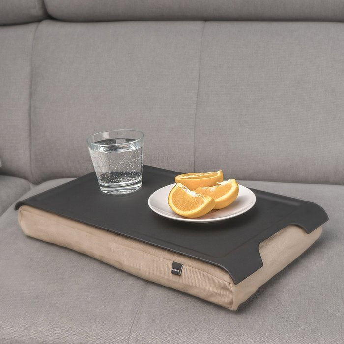Bricka med kudde på en grå soffa, med ett glas vatten och apelsinskivor på den svarta ytan