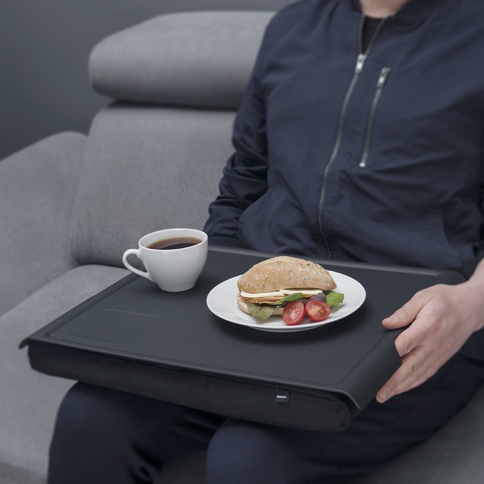 Person använder den svarta brickan med kudde för en måltid med smörgås och kaffe i soffan