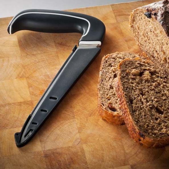 Ergonomisk brödkniv i svart knivfodral, ligger på en träskärbräda bredvid skivat bröd