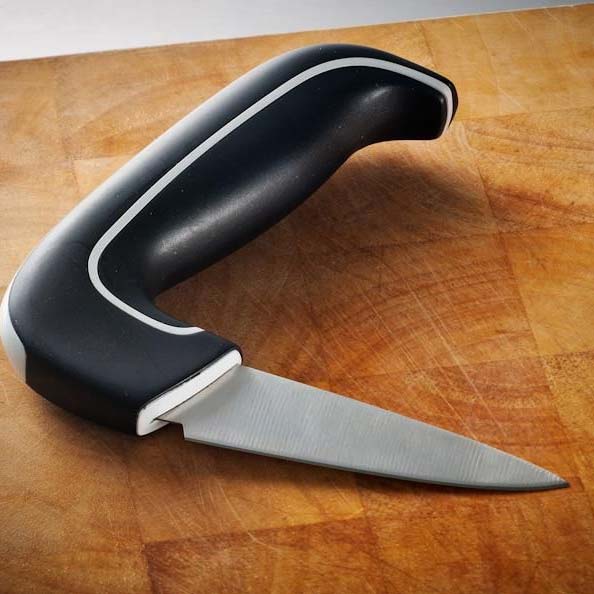 Ergonomisk grönsakskniv med svart halkfritt handtag och vit kant, liggande på en träskärbräda