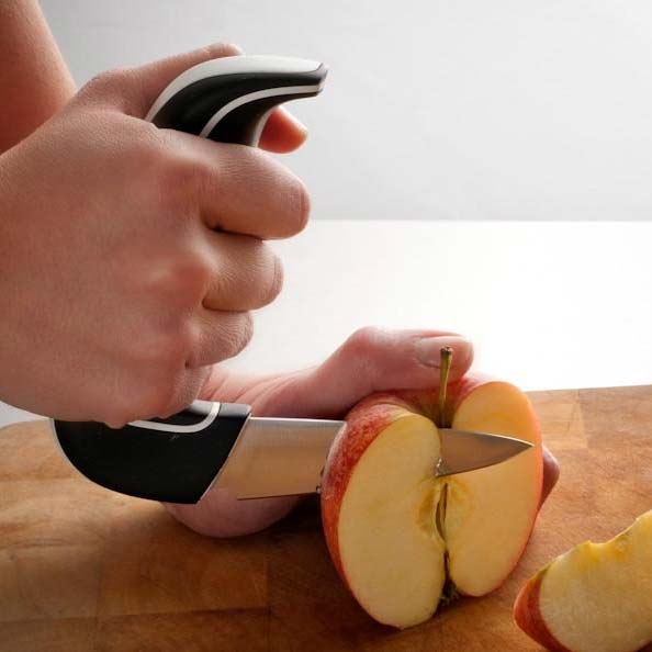 Händer håller den ergonomiska grönsakskniven med halkfritt grepp för att skära ett rött äpple
