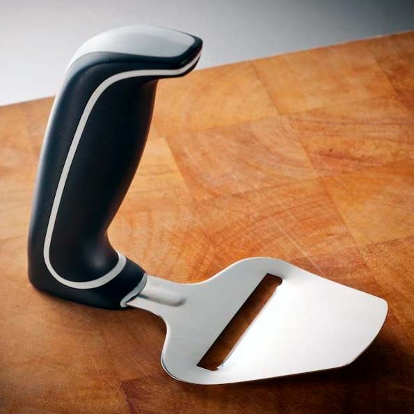 Ergonomisk osthyvel med svart och grått handtag och stålblad, liggande på en träskärbräda