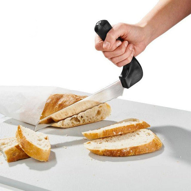 En hand använder den ergonomiska brödkniven med vinklat handtag för att skära en baguette på en skärbräda