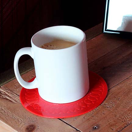 Rött runt halkskydd för kopp med en vit kaffekopp stående på ett träbord, sett från sidan