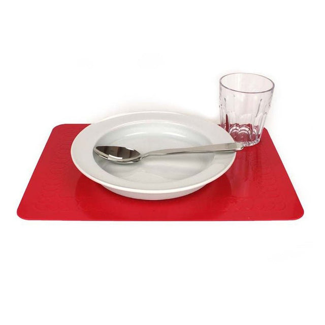 Rött halkfritt underlägg i silikon med en vit tallrik, sked och ett glas placerade ovanpå