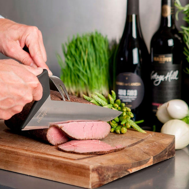 Person skär kött med den ergonomiska kockkniven och en stekgaffel på en träskärbräda