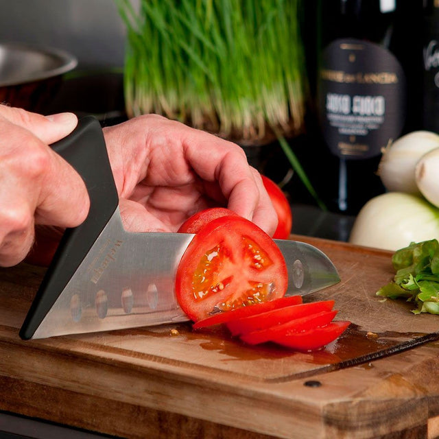 En hand som använder den ergonomiska grönsakskniven för att skära en tomat på en träskärbräda
