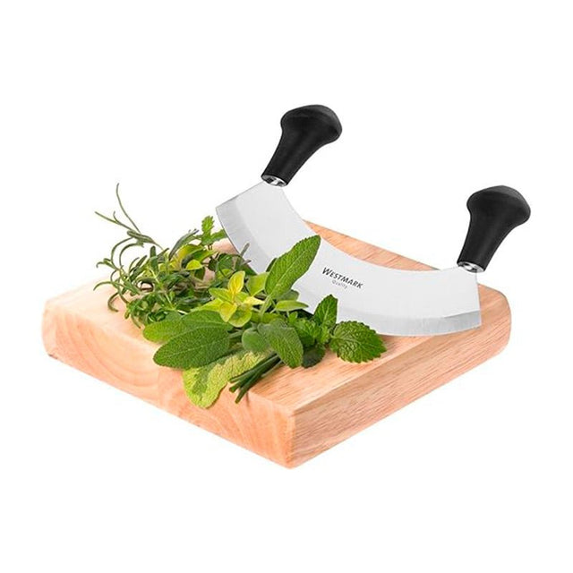 Örtvagga med böjt blad och svarta handtag placerad på en träskärbräda bredvid färska örter