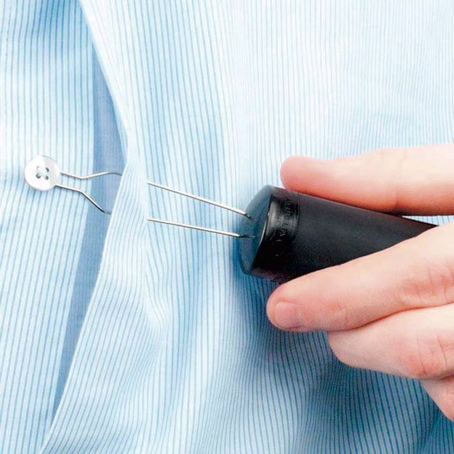 En hand använder knappknäpparen för att knäppa en vit knapp på en blårandig skjorta