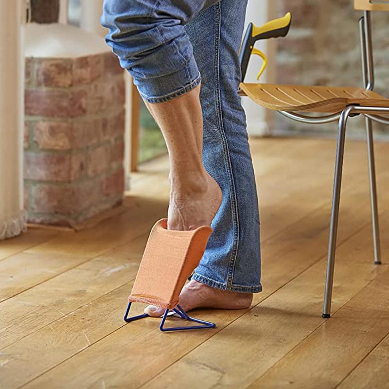 En person står och sätter foten i en orange strumpa på det blå strumpstativet