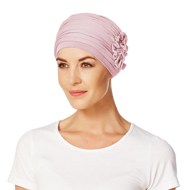 Modell visar en mjuk rosa Lotus turban från Christine Headwear, med dekorativ blomma