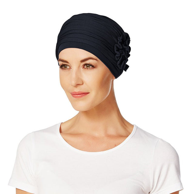 Modell bär en mörkblå Christine Headwear Lotus turban med elegant veckning och sidoblomma