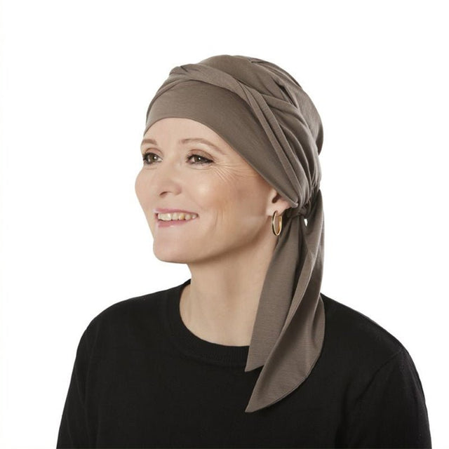 Kvinna med brun B.B. Beatrice turban, leende i sidoprofil mot vit bakgrund